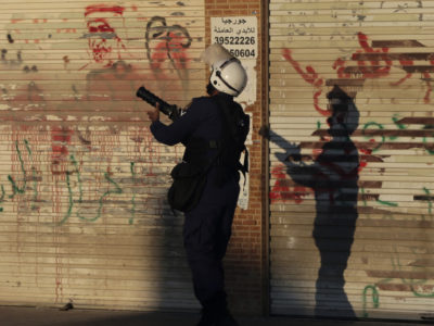 A riot policeman fires tear gas toward Bahraini anti-government protesters in Daih, Bahrain, on Saturday. Layers of anti-government graffiti are seen on shuttered storefronts as businesses in opposition areas nationwide observed a general strike in the run-up to Sunday's fifth anniversary of Bahrain's Arab Spring uprising. (AP Photo by Hasan Jamali)