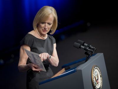 Judy Woodruff, anchor of the PBS NewsHour, holds up photograph while speaking at the Newseum in Washington, Friday, Oct. 10, 2014, during a memorial service for James S. Brady, former White House press secretary to President Ronald Reagan. (AP Photo/Pablo Martinez Monsivais)
