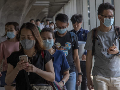 People wear face masks and check their phones in Thailand. (AP Photo/Gemunu Amarasinghe)