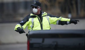 A Denver Police Department officer wears a surgical mask while directing traffic at a corona virus drive-through testing site outside the Denver Coliseum Saturday, March 14, 2020, in Denver. Officials planned to administer 150 tests but the line of vehicles wrapped around three city blocks. (AP Photo/David Zalubowski)