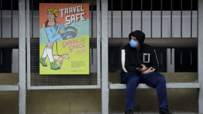 A bus rider wearing a face mask waits at a stop, March 16, in Santa Ana, California. (AP Photo/Chris Carlson)