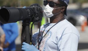 A photojournalist wears a mask and gloves as he covers a news conference in Miami on Sunday. (AP Photo/Wilfredo Lee)