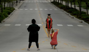 A woman wearing graduation attire is photographed in the middle of an empty street on the University of Kansas campus. (AP Photo/Charlie Riedel)