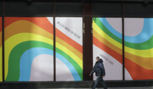 A man wearing a face mask walks past a window display of rainbows and signs that say "well get through this together" in the windows of the famous London department store Harrods in London, March 31. (AP Photo/Kirsty Wigglesworth)