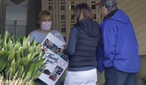 A worker wearing a mask holds a poster that was dropped off along with some Girl Scout cookies at the Life Care Center in Kirkland, Wash., Thursday, April 2, 2020. (AP Photo/Ted S. Warren)
