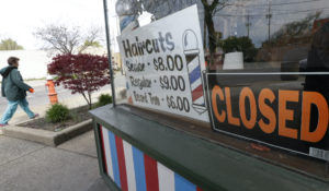 A woman walks past a closed barber shop, Wednesday, May 6, 2020, in Cleveland. (AP Photo/Tony Dejak)