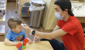 Aaron Rainboth, a teacher at the Frederickson KinderCare daycare center in Tacoma, Washington, wears a mask as he takes the temperature of Benjamin Simpson, 4. (AP Photo/Ted S. Warren)