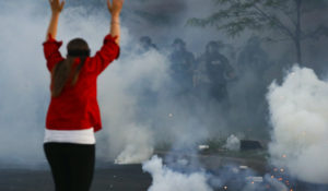 Tear gas canisters detonate beside a protester as authorities clear an intersection near the Minneapolis 5th Police Precinct, Saturday, May 30, 2020, in Minneapolis.  In Washington, D.C., authorities have disputed that they used "tear gas." (AP Photo/John Minchillo)