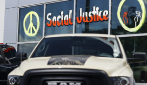 In this Sunday, June 7, 2020, photograph, an unsold 2020 pickup truck sits under a message written on the windows of a Ram dealership in Littleton, Colorado. (AP Photo/David Zalubowski)