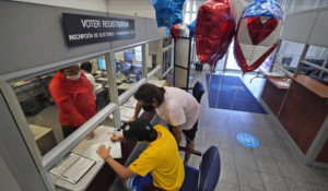 Lucas Saez, 22, fills out his voter registration form as his father Ramiro Saez, center rear, looks on at the Miami-Dade County Elections Department in Doral, Florida. (AP Photo/Wilfredo Lee)