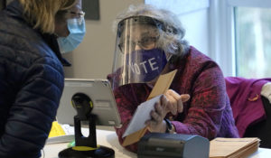 Poll worker Alice Machinist, of Newton, Mass., right, wears a mask and shield out of concern for the coronavirus while assisting a voter, left, with a ballot during early in-person general election voting, Wednesday, Oct. 28, 2020, in Newton, Mass. (AP Photo/Steven Senne)