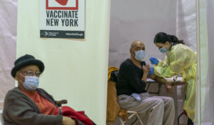 Registered Nurse Rita Alba, right, vaccinates a patient as another patient sits in the recovery area after being vaccinated at a pop-up COVID-19 vaccination site at the Bronx River Community Center, Jan. 31, 2021, in the Bronx. (AP Photo/Mary Altaffer)