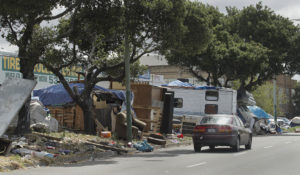 A car passes by a roadside homeless encampment in Oakland, California, in 2019. (AP Photo/Ben Margot)