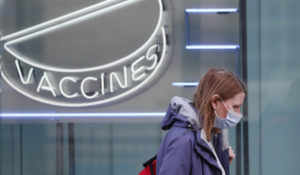 A woman wearing a mask walks past a neon sign display at the Wellcome Institute in London, Tuesday, Feb. 2, 2021. British health authorities plan to test tens of thousands of people in a handful of areas of England in an attempt to stop a new variant of the coronavirus first identified in South Africa spreading in the community. (AP Photo/Alastair Grant)