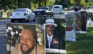 A procession of vehicles drive past photos of Detroit victims of COVID-19, Monday, Aug. 31, 2020 on Belle Isle in Detroit. (AP Photo/Carlos Osorio)