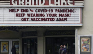 People walk below a sign on the marquee of the Grand Lake Theater advising people to wear masks and get vaccinated during the coronavirus pandemic in Oakland, Calif., Tuesday, March 9, 2021. (AP Photo/Jeff Chiu)