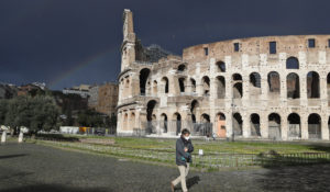 A man wearing a face mask to curb the spread of COVID-19 walks past Rome's ancient Colosseum as a rainbow appears, Monday, March 15, 2021. Half of Italy's regions have gone into the strictest form of lockdown in a bid to curb the latest spike in coronavirus infections that have brought COVID-19 hospital admissions beyond manageable thresholds. (AP Photo/Alessandra Tarantino)