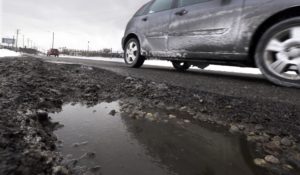 In this Wednesday, Feb. 18, 2015 file photo, a vehicle moves past a large pothole on Oakland Ave in Highland Park, Mich. $625 billion of a $2.25 trillion infrastructure stimulus bill being considered by Congress would go toward highways, bridges, ports, airlines, water systems and transit agencies. (AP Photo/Carlos Osorio, File)