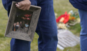 Joe Woodmansee holds a photo of the last time he and his three siblings were together with their mother, Carole Rae Woodmansee, as he visits Carole's grave, Saturday, March 27, 2021, at Union Cemetery in Sedro-Woolley, Wash., north of Seattle, prior to a memorial service. Carole died March 27, 2020 — the day of her 81st birthday — from complications of COVID-19 after contracting it during a choir practice that sickened 53 people and killed two. (AP Photo/Ted S. Warren)