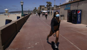 A woman wears a mask as she rides a skateboard along a beach promenade Tuesday, April 27, 2021, in San Diego. U.S. health officials say fully vaccinated Americans don't need to wear masks outdoors anymore unless they are in a big crowd of strangers. And unvaccinated people can drop face coverings in some cases, too. (AP Photo/Gregory Bull)