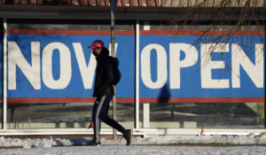 A pedestrian in a face covering walks past a sign plastered on the windows of a restaurant announcing that it is open on Feb. 25, 2021, in Boulder, Colo. (AP Photo/David Zalubowski)