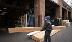 A worker wearing a mask carries a plank at Midwood Lumber & Millwork, Wednesday, March 25, 2020 in New York. (AP Photo/Mark Lennihan)