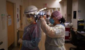 In this Dec. 22, 2020, file photo, registered nurse Dania Lima, right, helps fellow nurse Adriana Volynsky put on her personal protective equipment in a COVID-19 unit at Providence Holy Cross Medical Center in the Mission Hills section of Los Angeles. (AP Photo/Jae C. Hong, File)