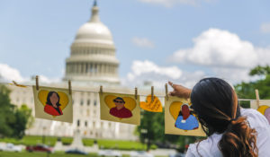 A supporter hangs signs commemorating family and friends who have died of COVID-19 at the Rally for Vaccine Access for Everyone, Everywhere on Wednesday, May 5, 2021 in Washington, D.C. (Eric Kayne/AP Images for Social Security Works)