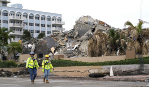 Workers walk past the collapsed and subsequently demolished Champlain Towers South condominium building, Tuesday, July 6, 2021, in Surfside, Fla. (AP Photo/Lynne Sladky)