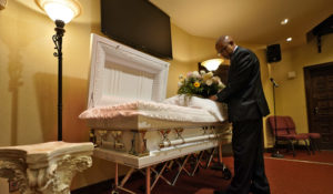Wayne Bright, funeral director at Wilson Funeral Home, arranges flowers on a casket before a service Thursday, Sept. 2, 2021, in Tampa, Fla.   Bright has seen grief piled upon grief during the latest COVID-19 surge as Florida is in the grip of its deadliest wave since the pandemic began, a disaster driven by the highly contagious delta variant. (AP Photo/Chris O'Meara)