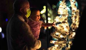 Allan Gubbins and his daughter Helena look at a Christmas tree during an outdoor Christmas Eve Service of Lights at the Granada Presbyterian Church, Thursday, Dec. 24, 2020, in Coral Gables, Fla. The service was held outdoors for safety reasons to protect against the spread of the coronavirus. (AP Photo/Lynne Sladky)