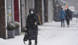 Pedestrians wear protective masks during the coronavirus pandemic as they walk along 71st Avenue as snow falls Thursday, Feb. 18, 2021, in the Queens borough of New York. Experts are looking at new COVID-19 outbreaks and forecasting a new winter surge this year. (AP Photo/Frank Franklin II)