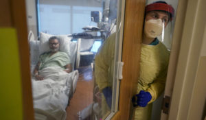 Registered nurse Rachel Chamberlin, of Cornish, N.H., right, steps out of an isolation room where where Fred Rutherford, of Claremont, N.H., left, recovers from COVID-19 at Dartmouth-Hitchcock Medical Center, in Lebanon, N.H., Monday, Jan. 3, 2022. Hospitals like this medical center, the largest in New Hampshire, are overflowing with severely ill, unvaccinated COVID-19 patients from northern New England. (AP Photo/Steven Senne)