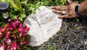 Octavia Tokley, the widow of Erin “Toke” Tokley, a Philadelphia  cop who died from COVID-19 in March, wipes a memorial stone in her garden, on Aug. 29, 2021, in Secane, Pa. Her husband was scheduled to be vaccinated on March 11 – which turned out to be his funeral. (AP Photo/Laurence Kesterson)
