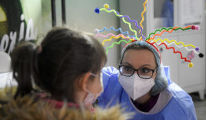 A member of the medical staff talks to a little girl as she waits to get her first dose of the Pfizer-BioNTech COVID-19  at a vaccination center in Bucharest, Romania, Wednesday, Jan.26, 2022. (AP Photo/Andreea Alexandru)