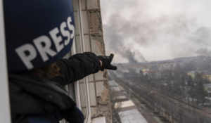 Associated Press photographer Evgeniy Maloletka points at the smoke rising after an airstrike on a maternity hospital, in Mariupol, Ukraine, Wednesday, March 9, 2022. (AP Photo/Mstyslav Chernov)