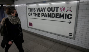 A woman wearing a face mask to curb the spread of coronavirus walks past a health campaign poster in an underpass leading to Westminster underground train station, in London, Thursday, Jan. 27, 2022. (AP Photo/Matt Dunham)