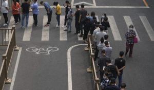 Residents and office workers wearing face masks line up on a road for mass coronavirus testing near the residential and commercial office complex at the central business district, Monday, April 25, 2022, in Beijing. (AP Photo/Andy Wong)