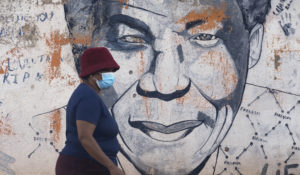 A woman wearing a mask walks past a mural of former South Africa's president Nelson Mandela, in Katlehong, east of Johannesburg, South Africa, Friday, April 29, 2022. South Africa's health minister says it is likely the country has entered a new wave of COVID-19 earlier than expected as new infections and hospitalizations have risen rapidly over the past two weeks. (AP Photo/Themba Hadebe)