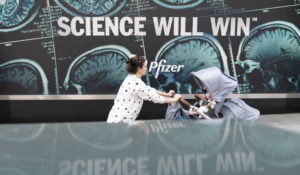 A woman pushes a baby in a stroller past a sign hanging outside Pfizer headquarters in New York, Monday, May 23, 2022. (AP Photo/Mary Altaffer)