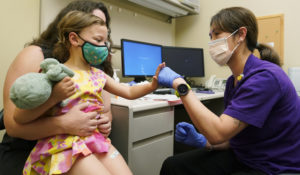 Nora Burlingame, 3, is held by her mother, Dina Burlingame, as she gives a fist-bump to nurse Luann Majeed, right, Tuesday, June 21, 2022, after getting a Pfizer COVID-19 vaccine shot at a University of Washington Medical Center clinic in Seattle. (AP Photo/Ted S. Warren)