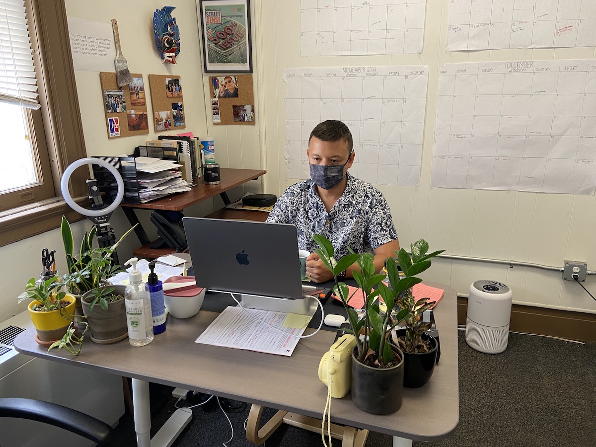 Man with face mask sitting behind a computer in a small office.