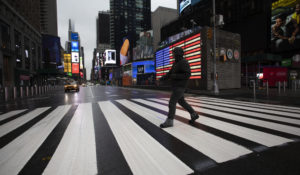 A man crosses the street in a nearly empty Times Square, which is usually very crowded on a weekday morning, Monday, March 23, 2020 in New York. Gov. Andrew Cuomo has ordered most New Yorkers to stay home from work to slow the coronavirus pandemic. (AP Photo/Mark Lennihan)