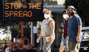 Pedestrians wear masks as they walk in front of a sign reminding the public to take steps to stop the spread of coronavirus, Thursday, July 23, 2020, in Glendale, Calif. (AP Photo/Chris Pizzello)