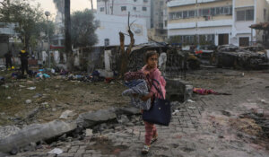 A girl carries blankets as she walks past the site of a deadly explosion at al-Ahli Hospital in Gaza City, Wednesday, Oct. 18, 2023. (AP Photo/Abed Khaled)