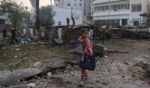 A Palestinian girl carries blankets on Wednesday as she walks past the site of a deadly explosion at al-Ahli hospital, in Gaza City. (AP Photo/Abed Khaled)