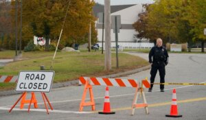 A police officer stands at a road closure near a bowling alley, seen in the background on Thursday in Lewiston, Maine. The site is one of Wednesday's two mass shootings in the city. (AP Photo/Robert F. Bukaty)