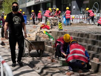 A foreman in black at left supervises workers renovating a walk way in front of a commercial building in Beijing, Tuesday, April 16, 2024. (AP Photo/Ng Han Guan)