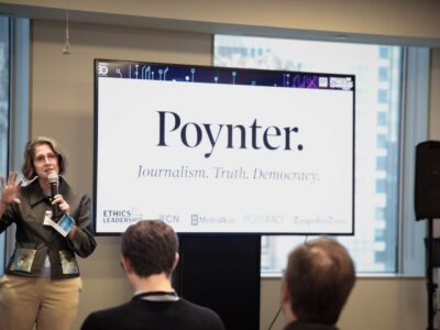 Kelly McBride stands in front of a screen speaking to a crowd at the AI Summit.