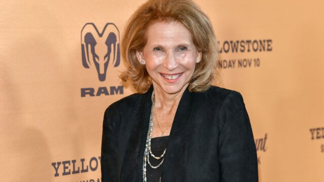 An older white woman in black suit smiles at the camera